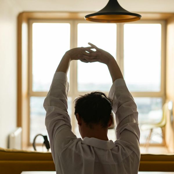 Man stretching calmly by a large window at sunrise.